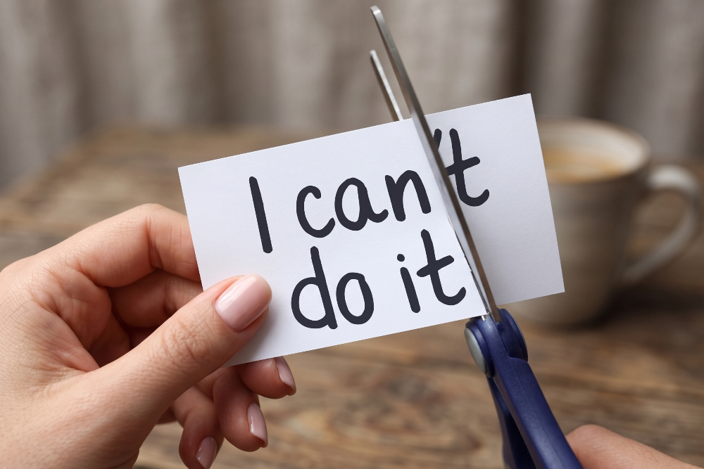 Building Confidence | Empower Me Hub Close-up of hands cutting a white card that reads 'I can't do it' with blue scissors.
